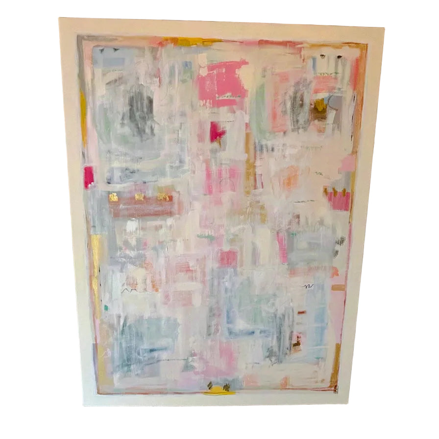 A large framed abstract painting with layered brushstrokes in pink, white, light blue, gray, and touches of yellow, displayed against a rustic red-brown brick wall.