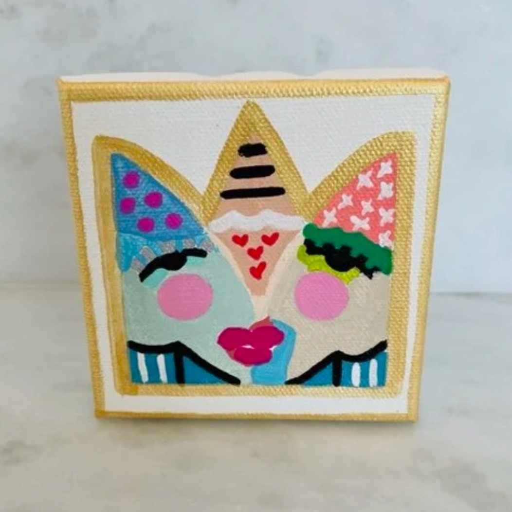 A square canvas art print featuring a whimsical, colorful illustration of three faces wearing party hats, displayed on a light marble surface against a light gray marble wall.