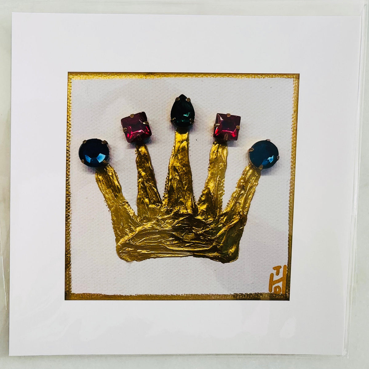 Two square white art prints displayed side-by-side on a light gray marble surface. Each print features a textured, crumpled gold crown with faceted gems on a thin gold border.