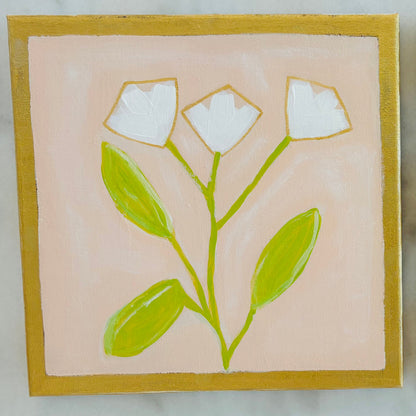 Two square hand-painted ceramic tiles featuring minimalist floral designs, displayed side-by-side on a light gray marble surface. The left tile depicts white flowers with green leaves on a soft pink background with a gold border.