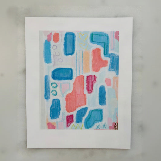 An abstract art print featuring colorful painted shapes in blue, pink, and orange on a white background, displayed on a light gray marble surface.