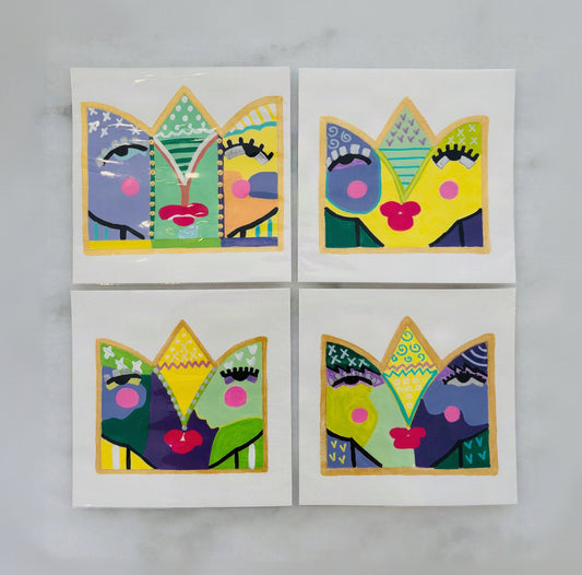 Four square art prints arranged in a 2x2 grid on a light marble surface. Each print features a colorful abstract face design inside a crown-like shape, using bright yellow, green, blue, purple, pink, and black patterns with gold outlines.