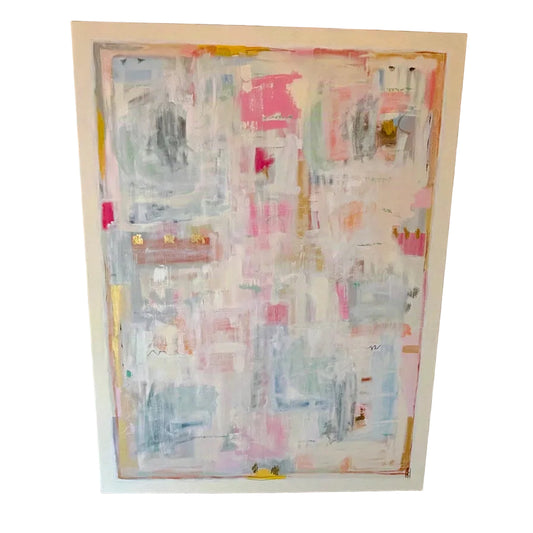 A large framed abstract painting with layered brushstrokes in pink, white, light blue, gray, and touches of yellow, displayed against a rustic red-brown brick wall.